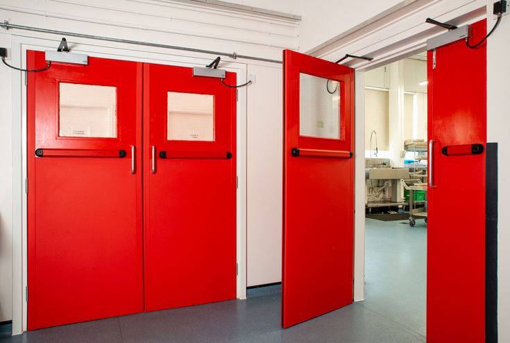 Fire Door & Safety Double red doors with windows, leading to a room beyond.