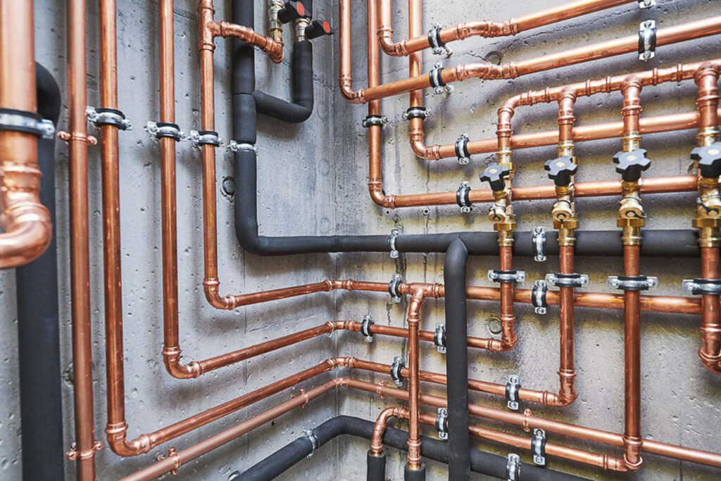Plumbing Copper and black pipes arranged in a complex network on a concrete wall.