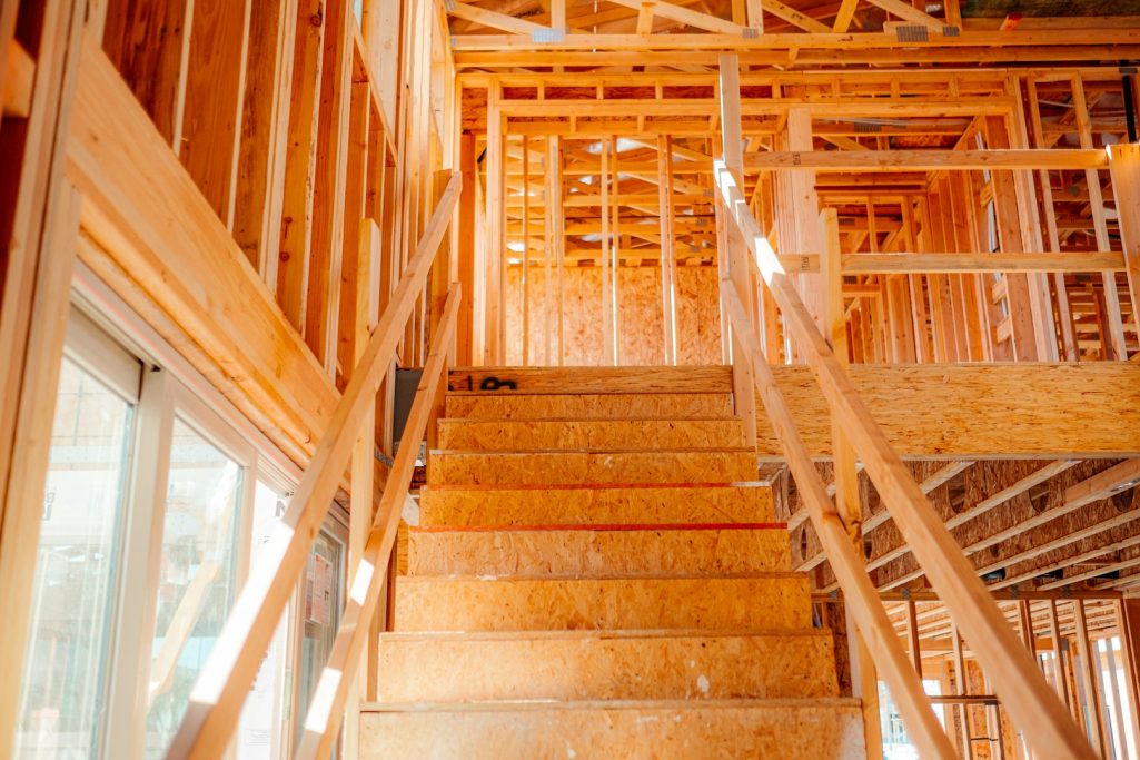 MDF Works Interior of a wooden house under construction, featuring exposed framing and a wooden staircase.