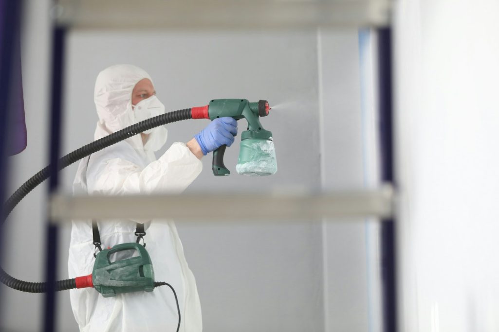 Painting Person in protective gear spraying paint with a spray gun.