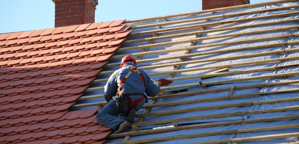 roofing Worker installing roof tiles on a sloped roof under a clear blue sky.
