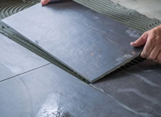 Tiling Floor & Wall Hands placing a slate tile onto a prepared adhesive surface.