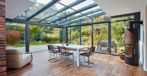 Home Renovation Modern conservatory with a glass roof, dining table, and views of a green garden.