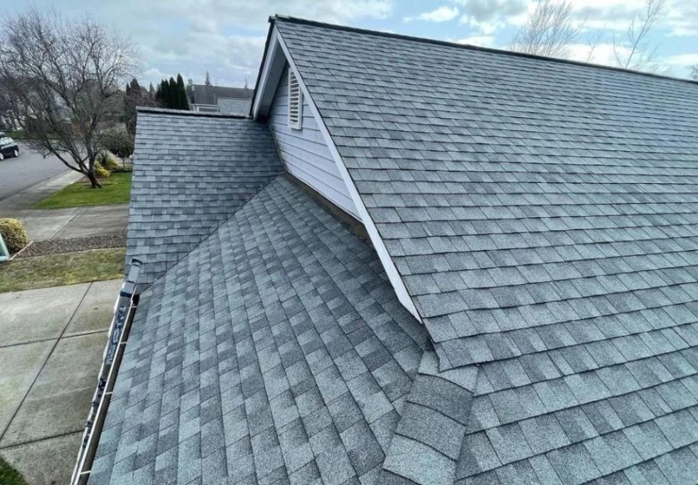 Roofing Grey asphalt shingles cover a sloped roof with a clear blue sky in the background.
